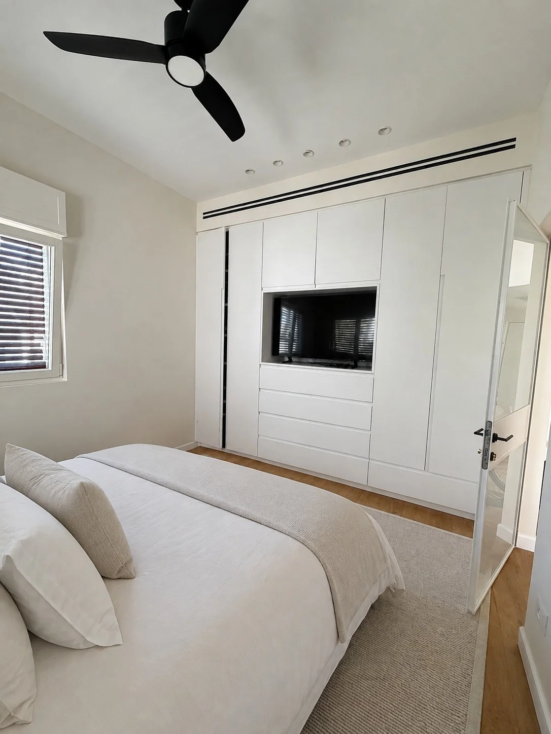 Chambre principale avec armoire blanche intégrée et télévision